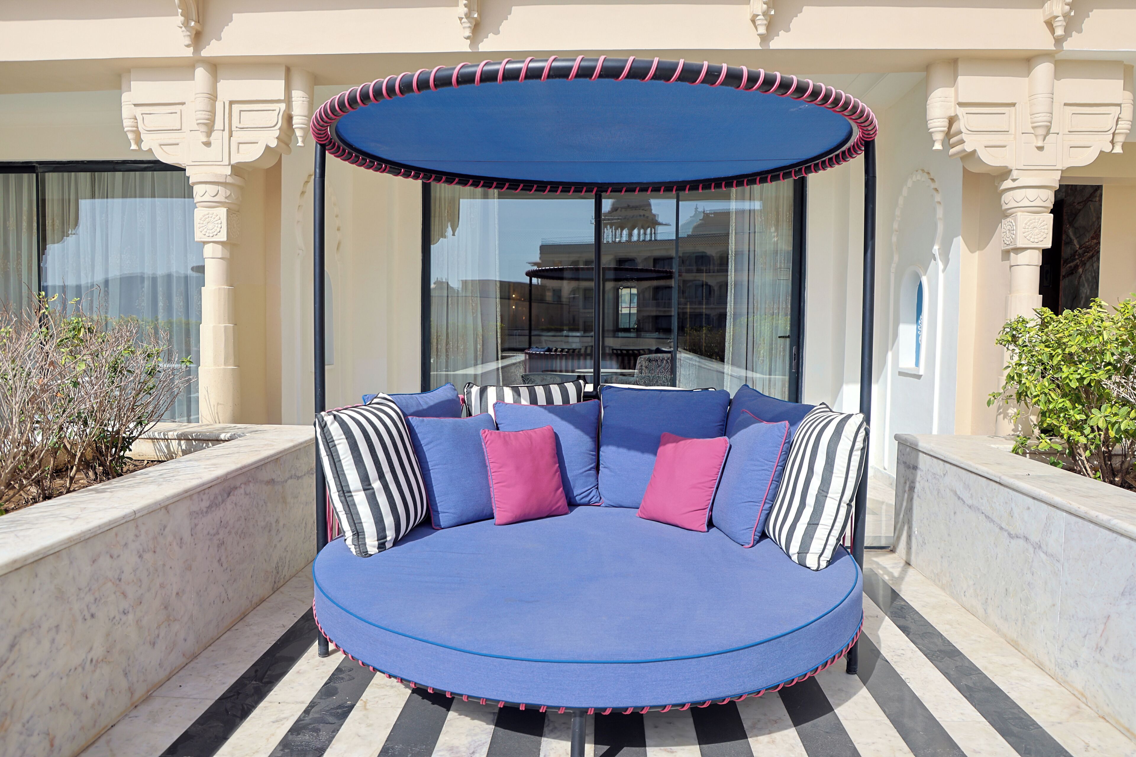 A circular outdoor seating area with a blue canopy, surrounded by marble steps and columns.