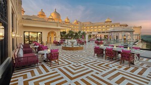 A hotel lobby with a patterned floor, seating areas, and a large building with domed structures in the background. - Fairmont Udaipur Palace (Udaipur)