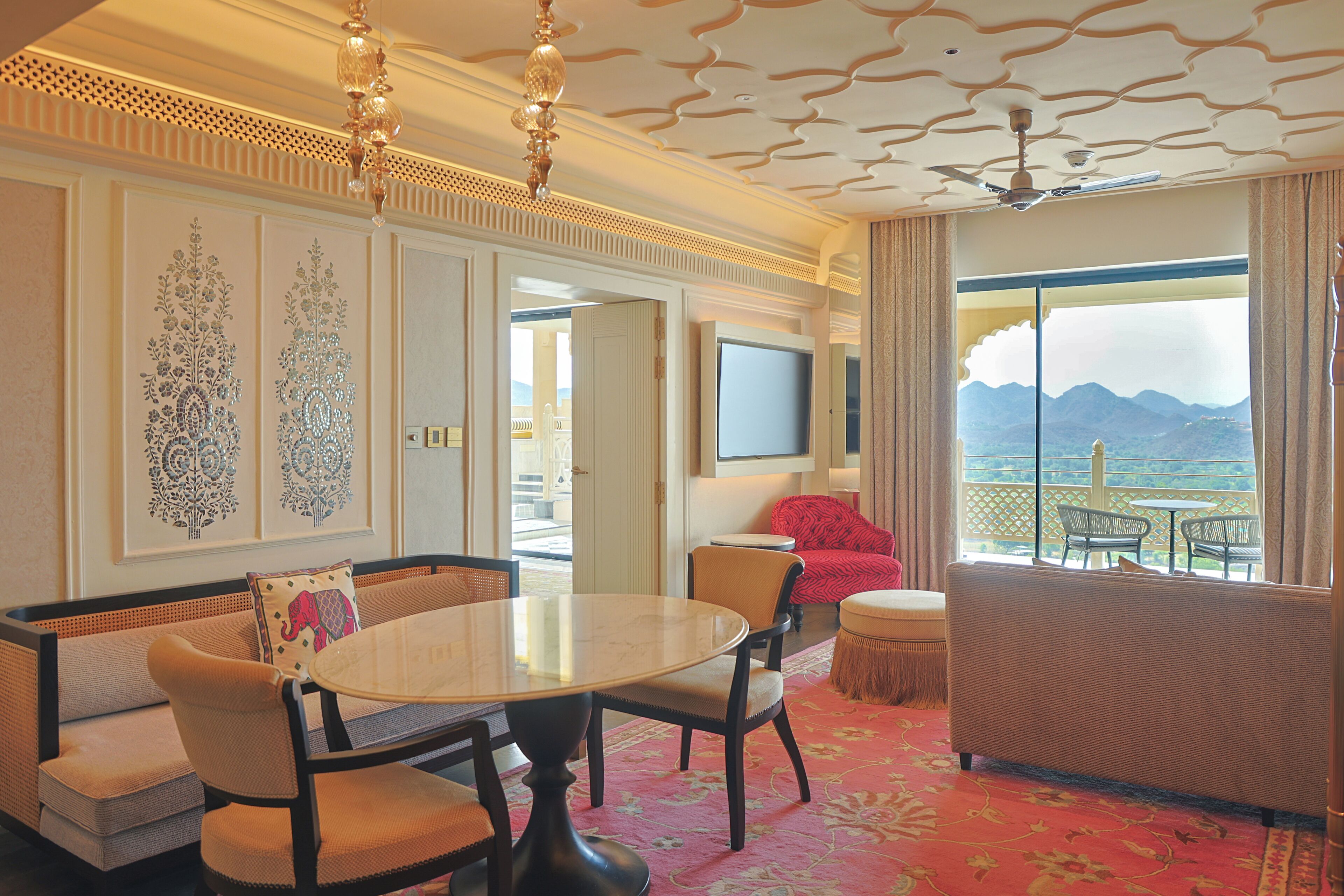 A hotel room with a dining area, a sofa, a TV, and a view of mountains.