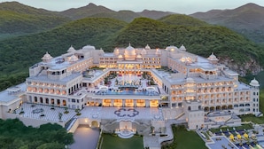 A large, multi-story hotel with a central courtyard, surrounded by lush greenery and hills. - Fairmont Udaipur Palace (Udaipur)