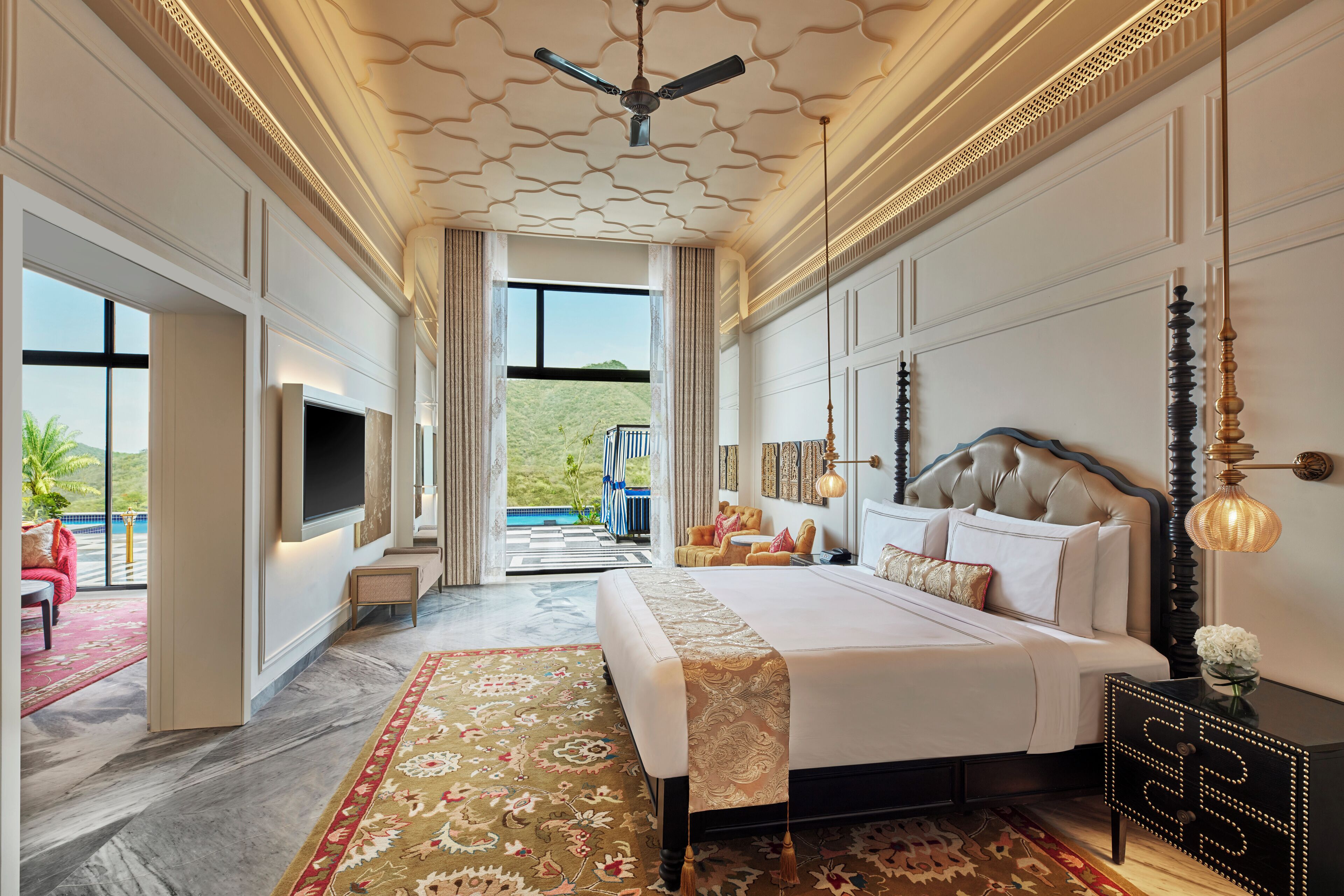 A spacious bedroom with a large bed, a television, and a view of a green landscape.