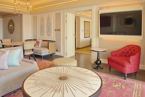 Amplia sala de estar con una mesa de centro redonda, un sillón rojo estampado y un sofá blanco con cojines decorativos.