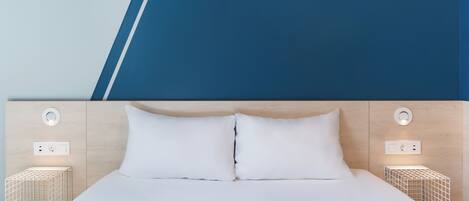 A modern hotel room with a large bed, two bedside tables with built-in lighting, and a wooden headboard.