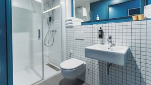 A modern bathroom with a glass-enclosed shower, a white toilet, and a sink with a mirror above it. - ibis Budget Madrid Albasanz (Madrid)
