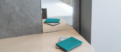 Una habitación de hotel con un escritorio de madera, una libreta azul turquesa y un teléfono inteligente.