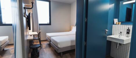 Una habitación de hotel moderna con una cama, un escritorio, una silla, una mesita, un lavabo y un espejo.