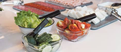 Una mesa de buffet con distintos alimentos, como pepinos en rodajas, tomates y lechuga.