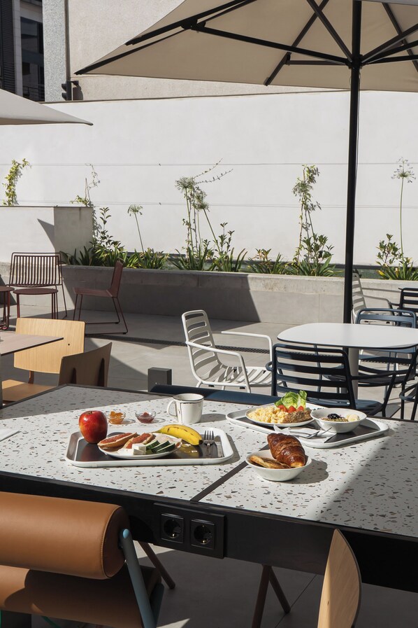 An outdoor dining area with tables, chairs, and a variety of food items. - ibis Budget Madrid Albasanz (Madrid)