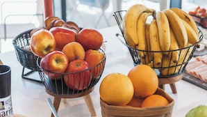 A table with a basket of apples, a basket of bananas, and a bowl of oranges.