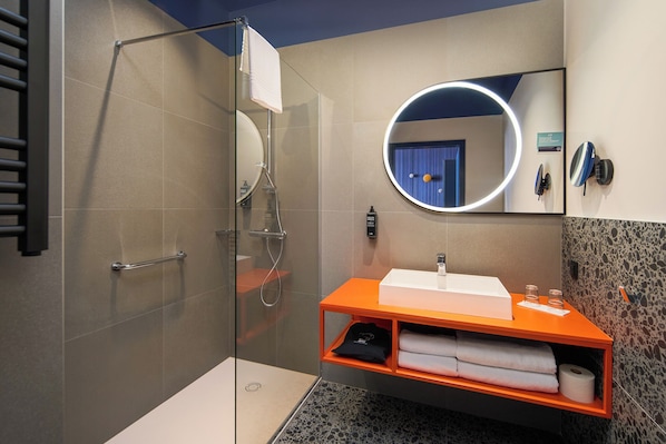 Un baño moderno con ducha envuelta en vidrio, un lavamanos blanco y un tocador naranja.