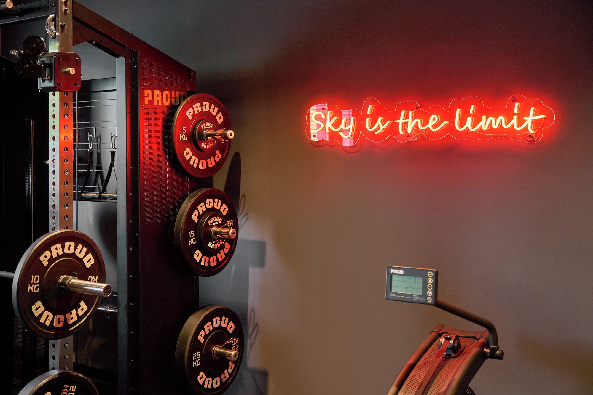A gym with weightlifting equipment and a motivational neon sign saying "Sky is the limit".