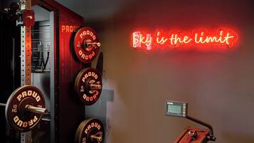 Un gimnasio con equipo de levantamiento de pesas y un letrero de neón motivacional que dice "Sky is the limit".