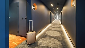Un couloir d’hôtel avec un sol recouvert de moquette, une valise et des portes de part et d’autre.
