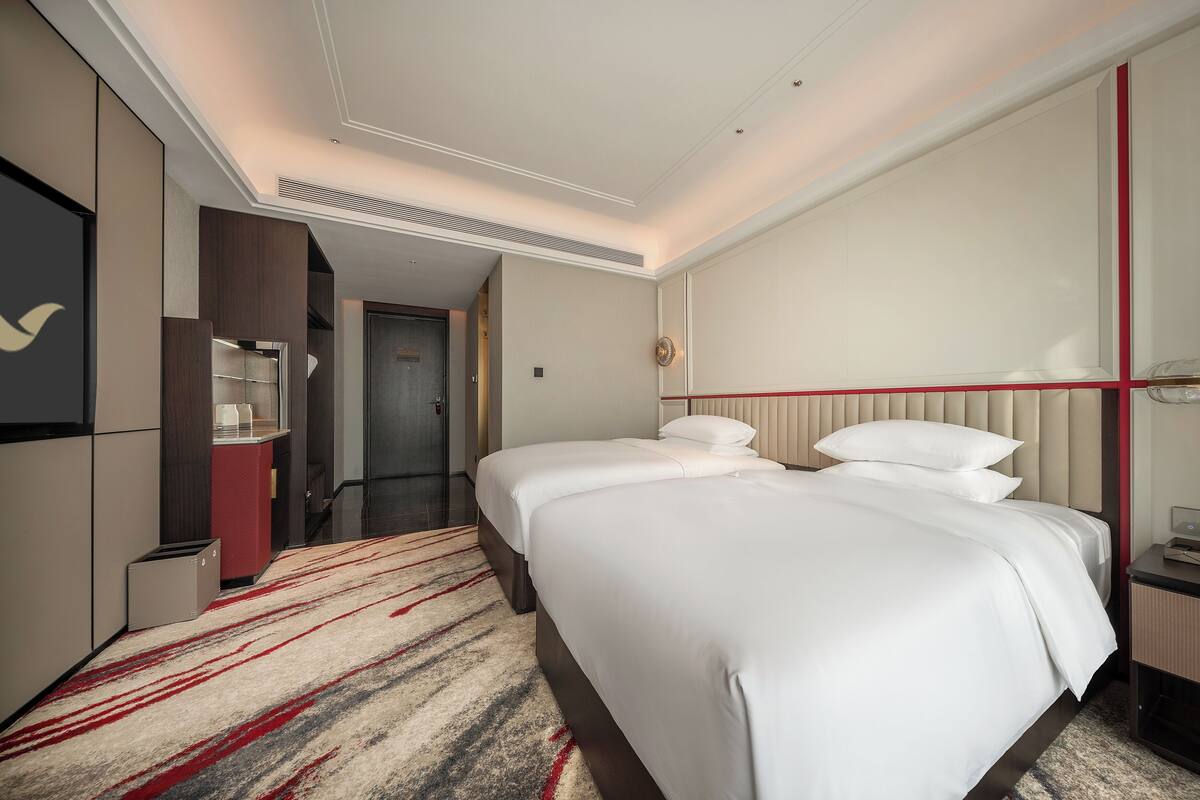 Quarto de hotel com duas camas, um armário vermelho, um espelho e piso coberto por carpete.