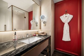 Un baño moderno con lavamanos de mármol, un espejo grande, una bata colgada en la pared y una pared de acento roja.