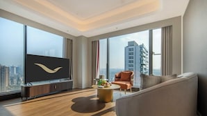 Ein modernes Wohnzimmer mit großem Fernseher, einer Couch, einem Couchtisch und Blick auf eine Stadtlandschaft durch große Fenster.