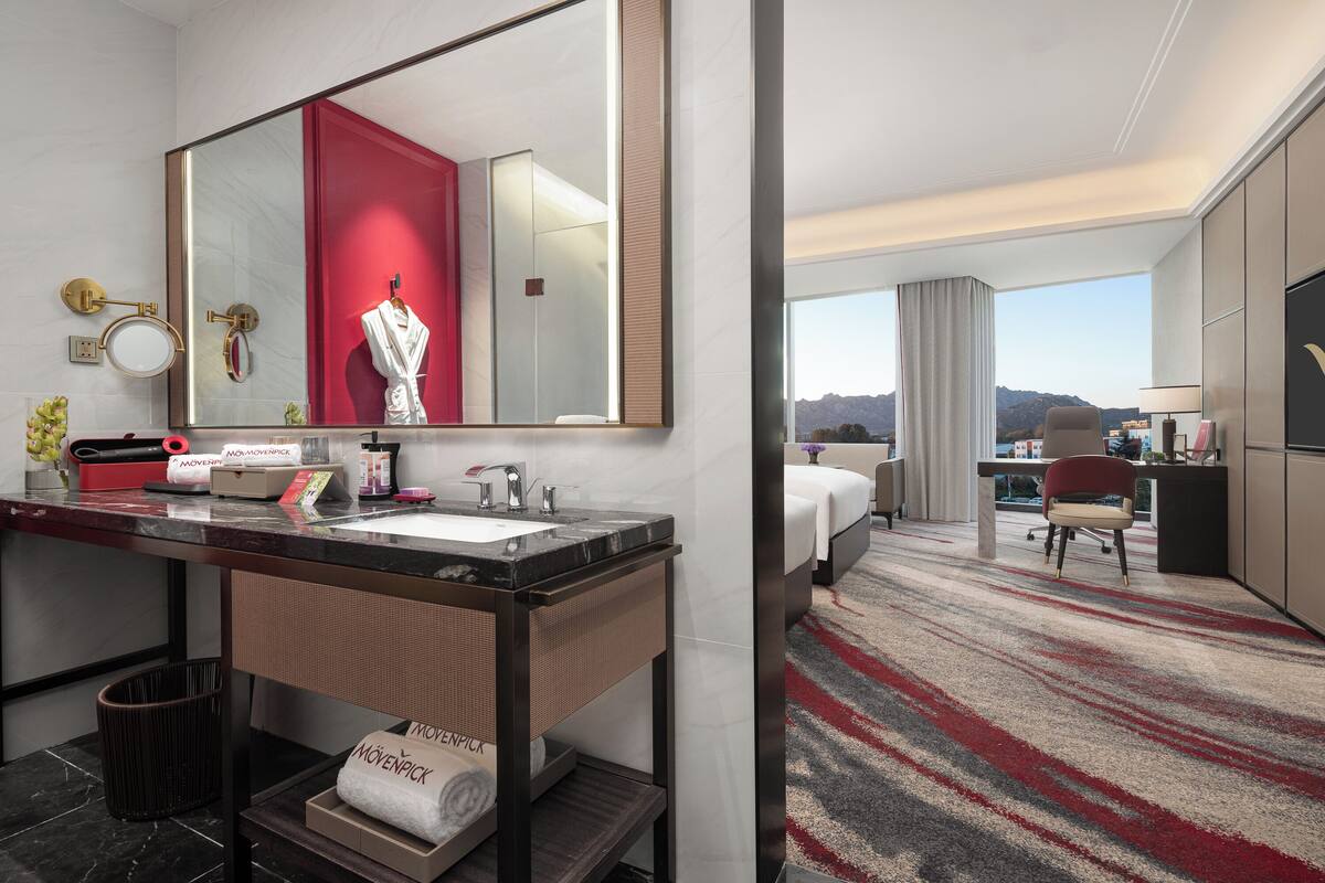 A hotel bathroom with a large mirror, a sink, and a robe hanging on a hook.