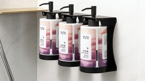 Three YUNI body wash dispensers mounted on a black stand against a white tiled wall. - Movenpick By Accor Qingdao Sunmei (Qingdao)