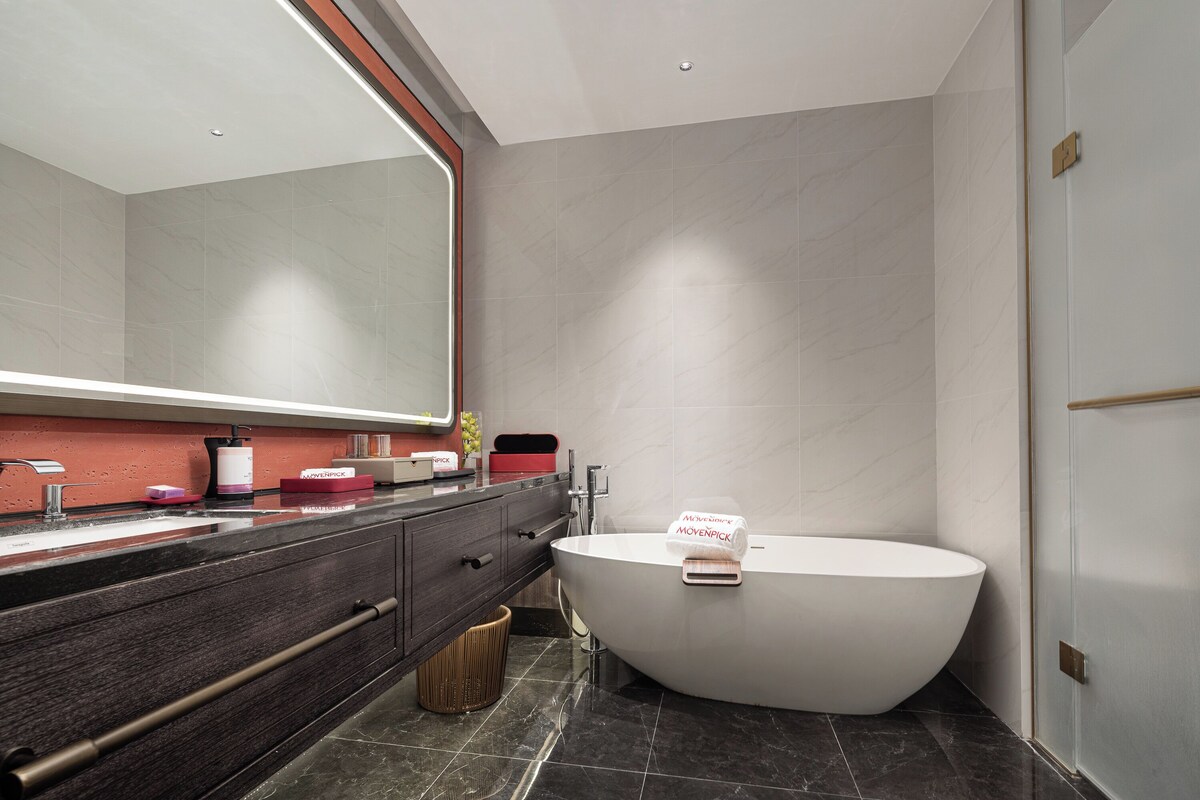 Un baño moderno con una bañera independiente, un espejo grande y un tocador de madera oscura.