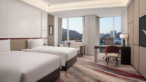 A hotel room with two beds, a desk, a chair, a TV, and a large window with a cityscape view. - Movenpick By Accor Qingdao Sunmei (Qingdao)