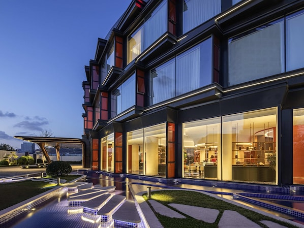 A modern hotel with large windows, a swimming pool, and a well-lit exterior.