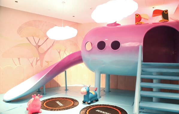 Zona de juegos infantiles con tobogán, estructura para escalar y un caballo de juguete.