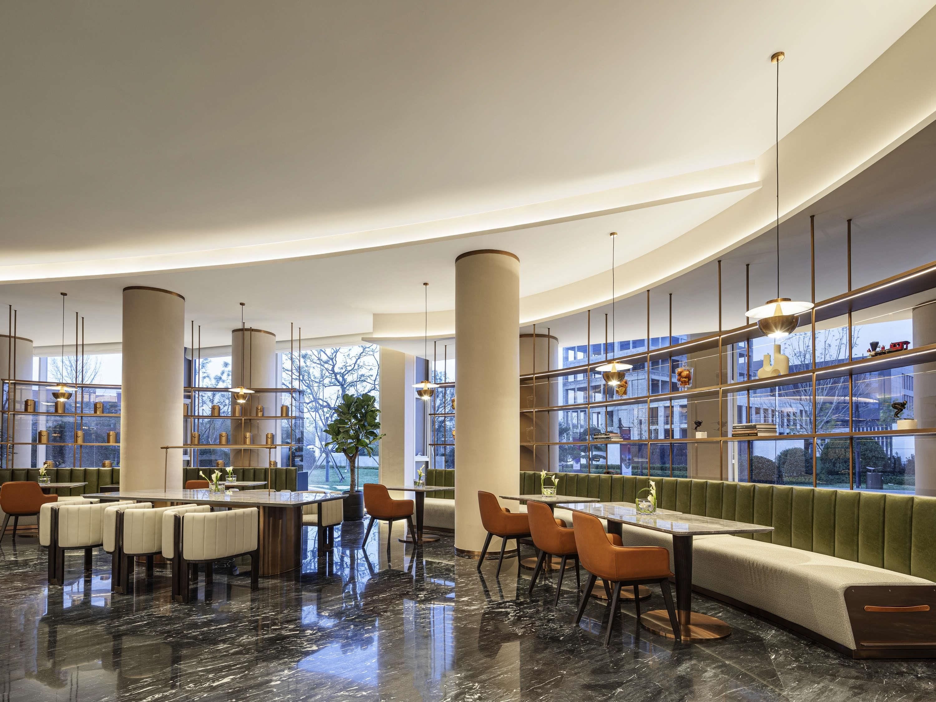 Um interior moderno com teto curvo, piso de mármore e área de estar com um banco estofado verde.
