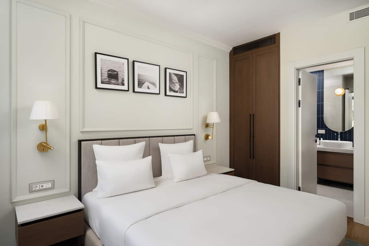 A hotel room with a bed, bedside lamps, a wardrobe, and a bathroom visible through an open door.