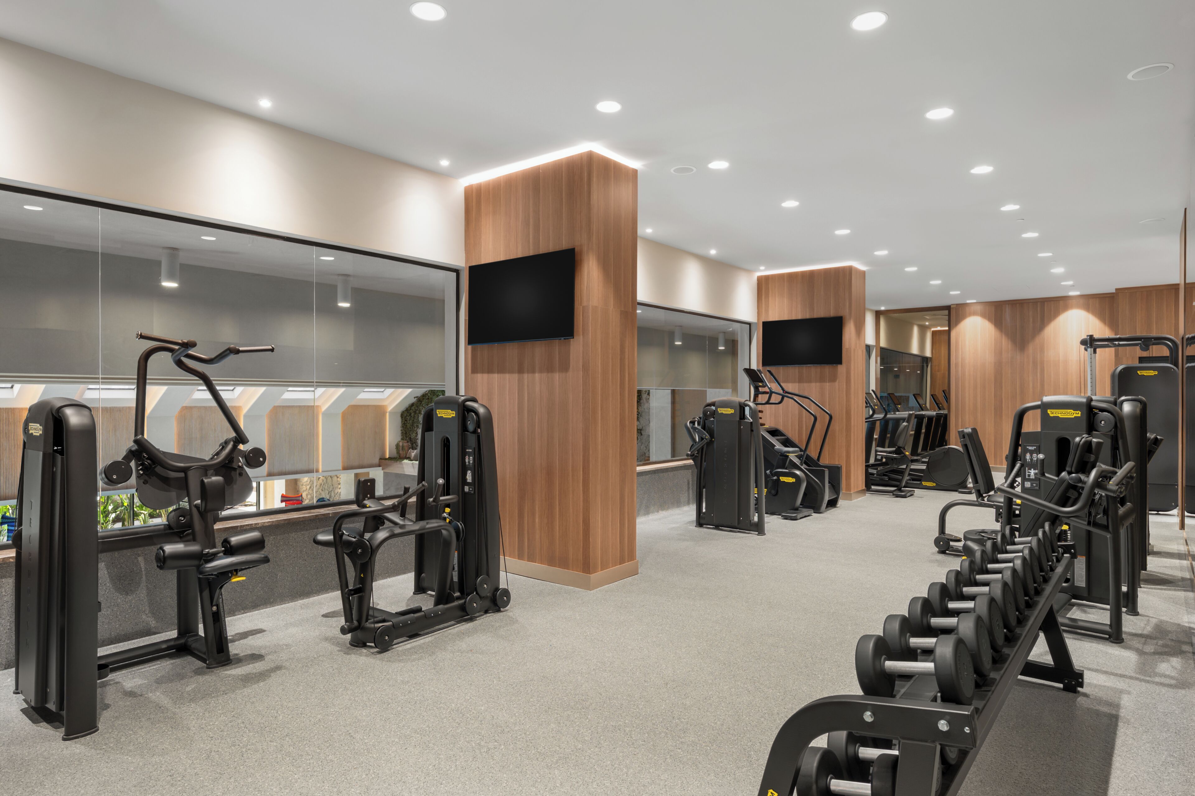 Un gimnasio moderno con diversos equipos de ejercicio, paneles de madera en las paredes y un espejo grande.