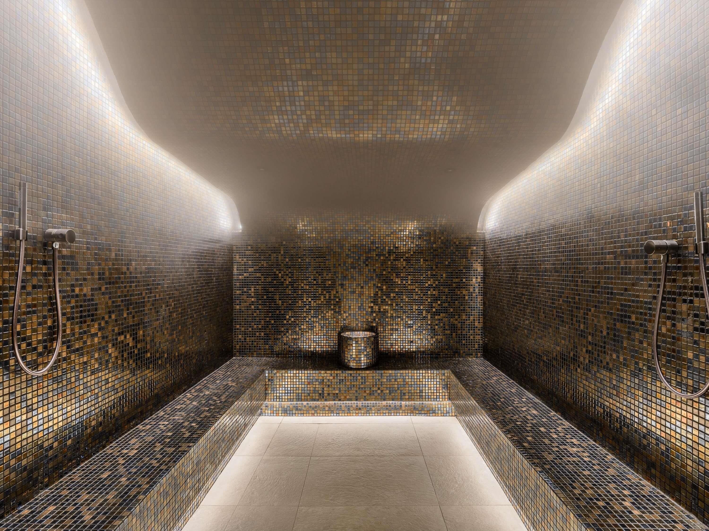 Une salle de bain moderne avec des murs recouverts de mosaïques, une baignoire centrale et deux pommes de douche.