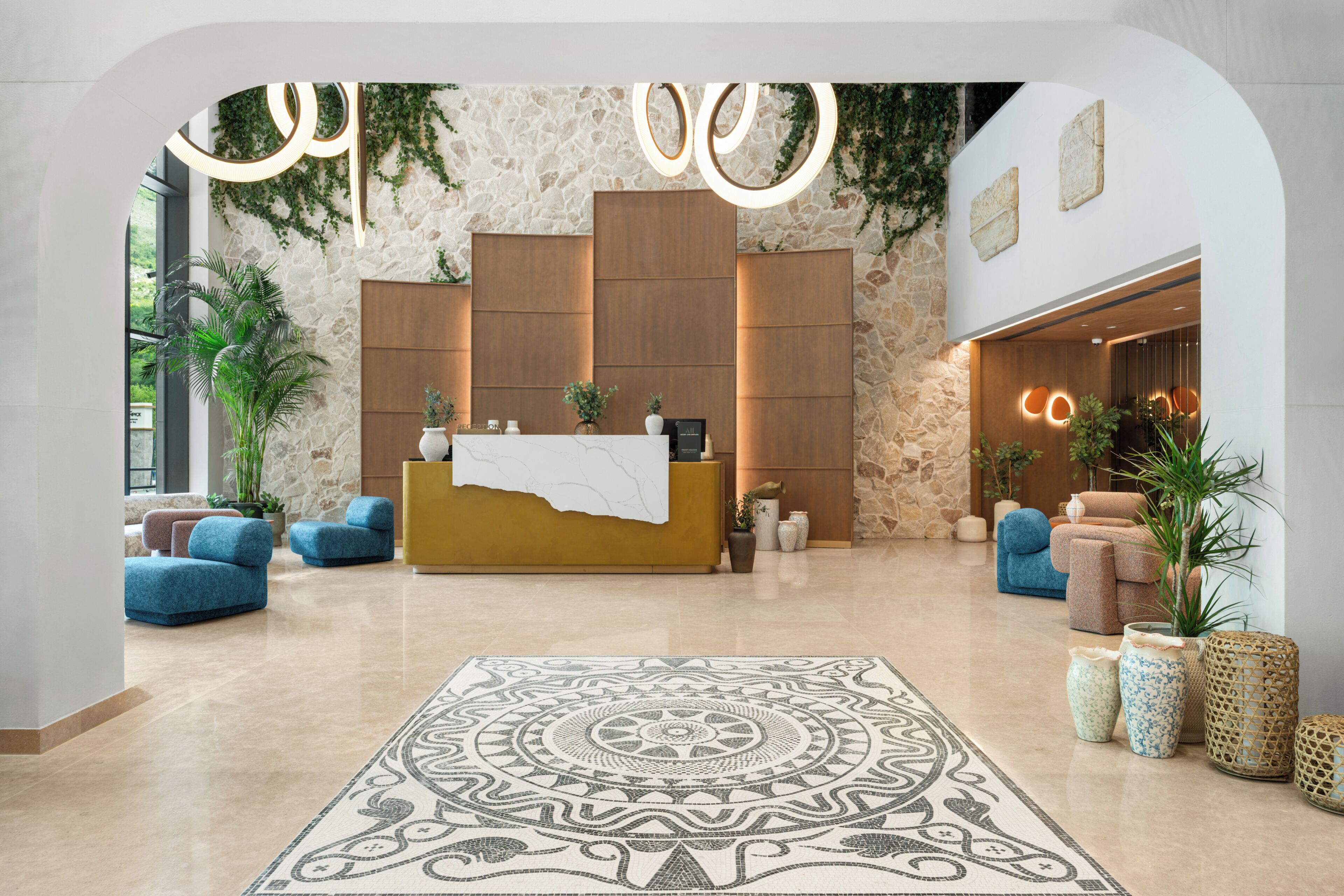 A reception area with a stone wall, wooden reception desk, blue sofas, and a patterned rug.