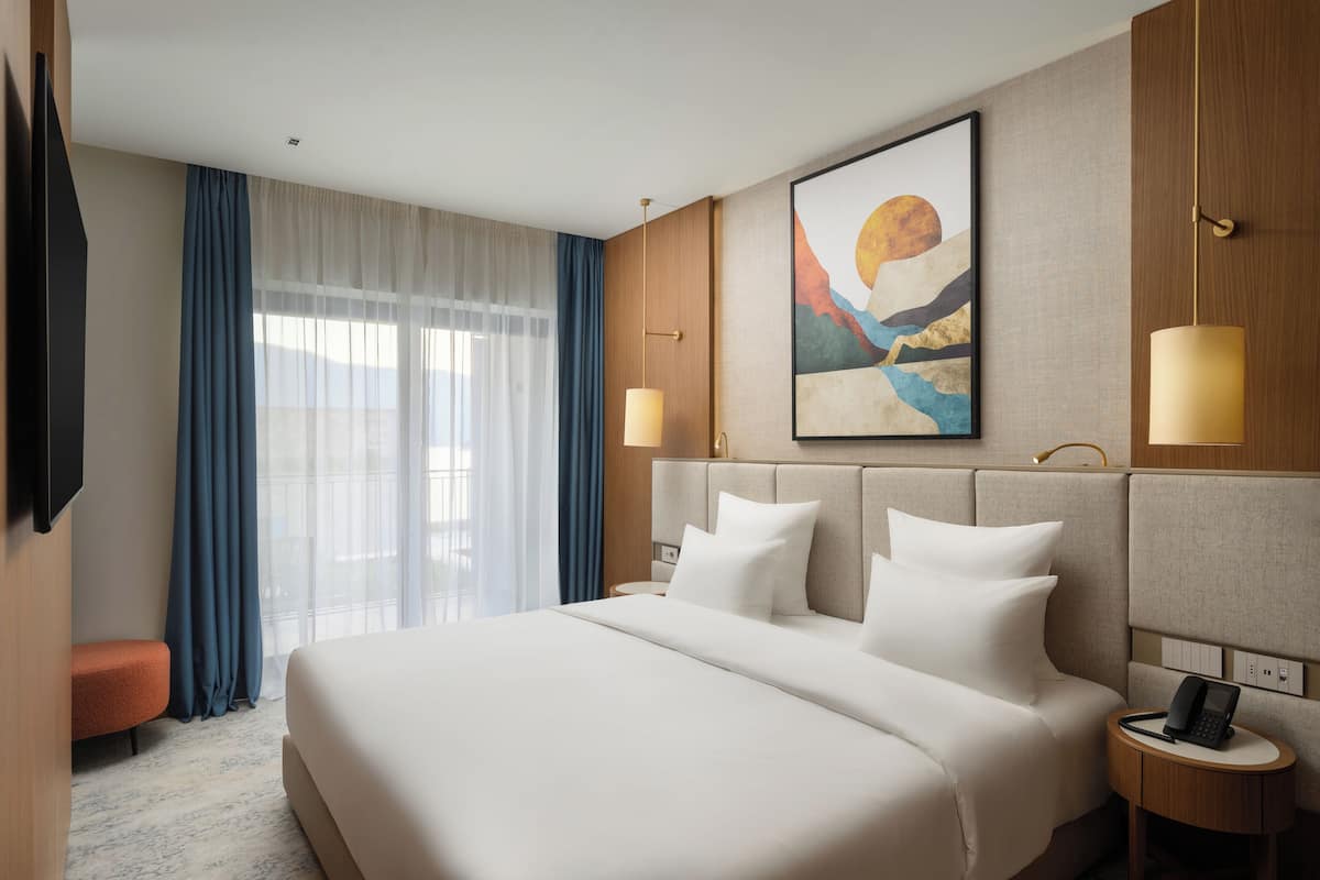 A hotel room with a large bed, a flat-screen TV, a bedside table with a lamp, and a painting on the wall.