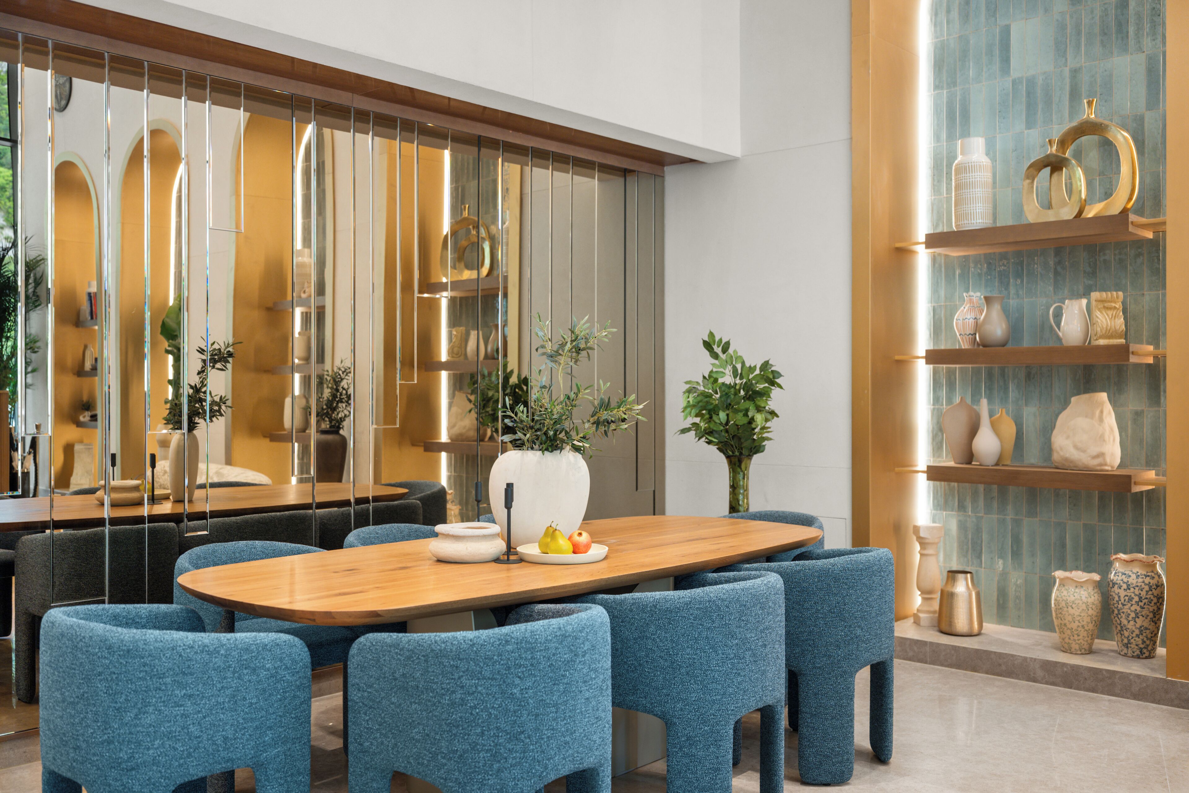 Un comedor moderno con una mesa de madera, sillas tapizadas en azul y jarrones decorativos en estantes.