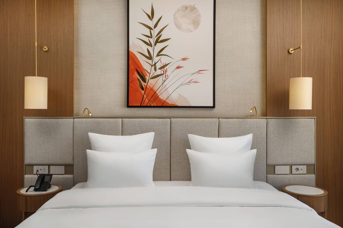 A hotel room with a bed, two bedside tables, a wall-mounted phone, and a framed artwork above the bed.