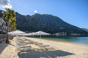 En strand med vita solstolar och parasoller, ett berg i bakgrunden och ett lugnt hav.