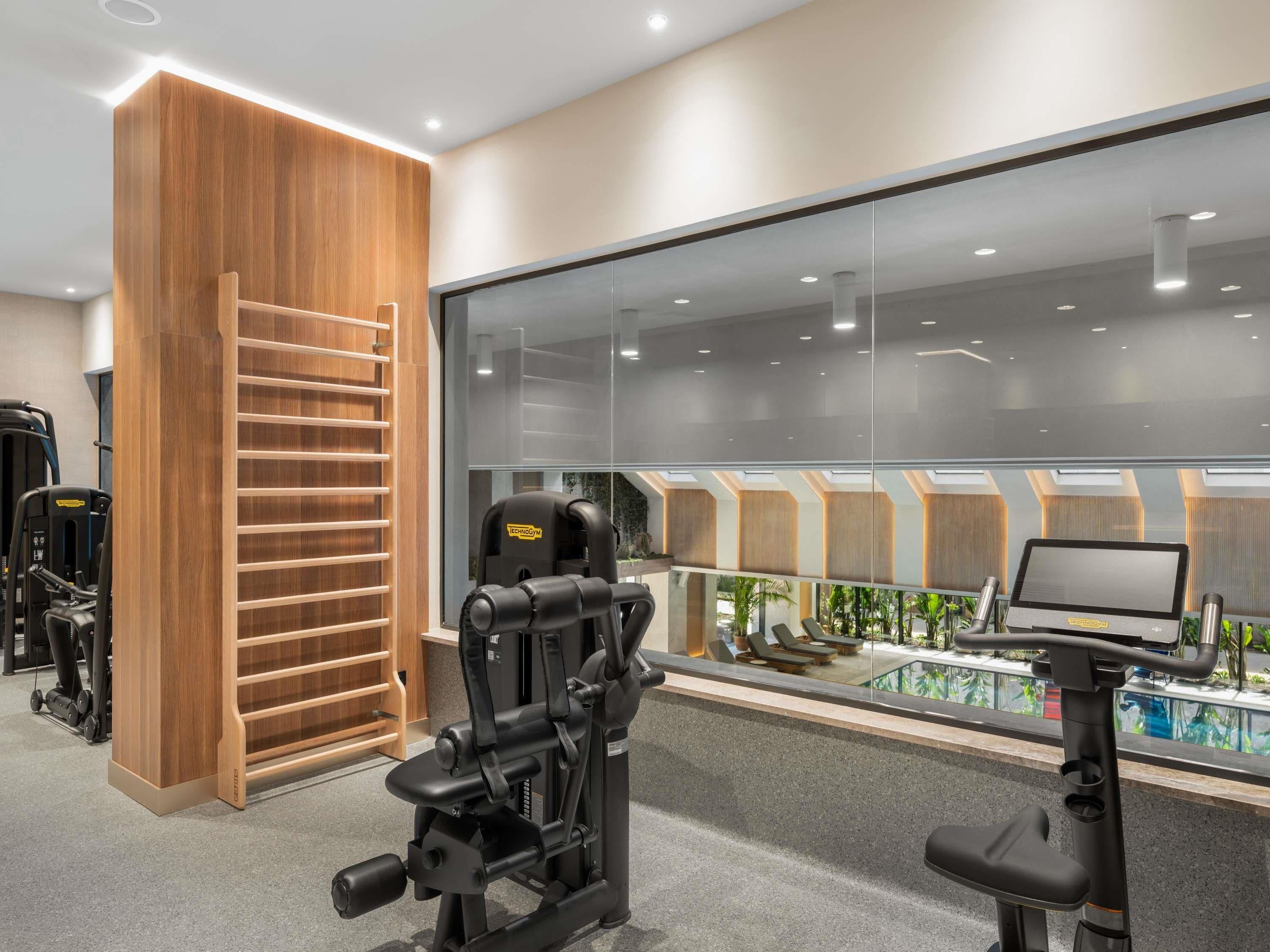 A modern gym with exercise equipment, a wooden wall, and a large window overlooking a pool area.