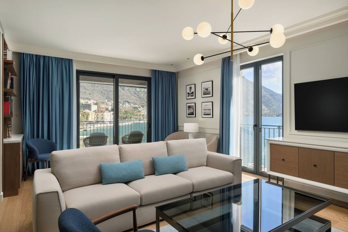 A modern living room with a sofa, a glass coffee table, and a view of a balcony with a mountain backdrop.