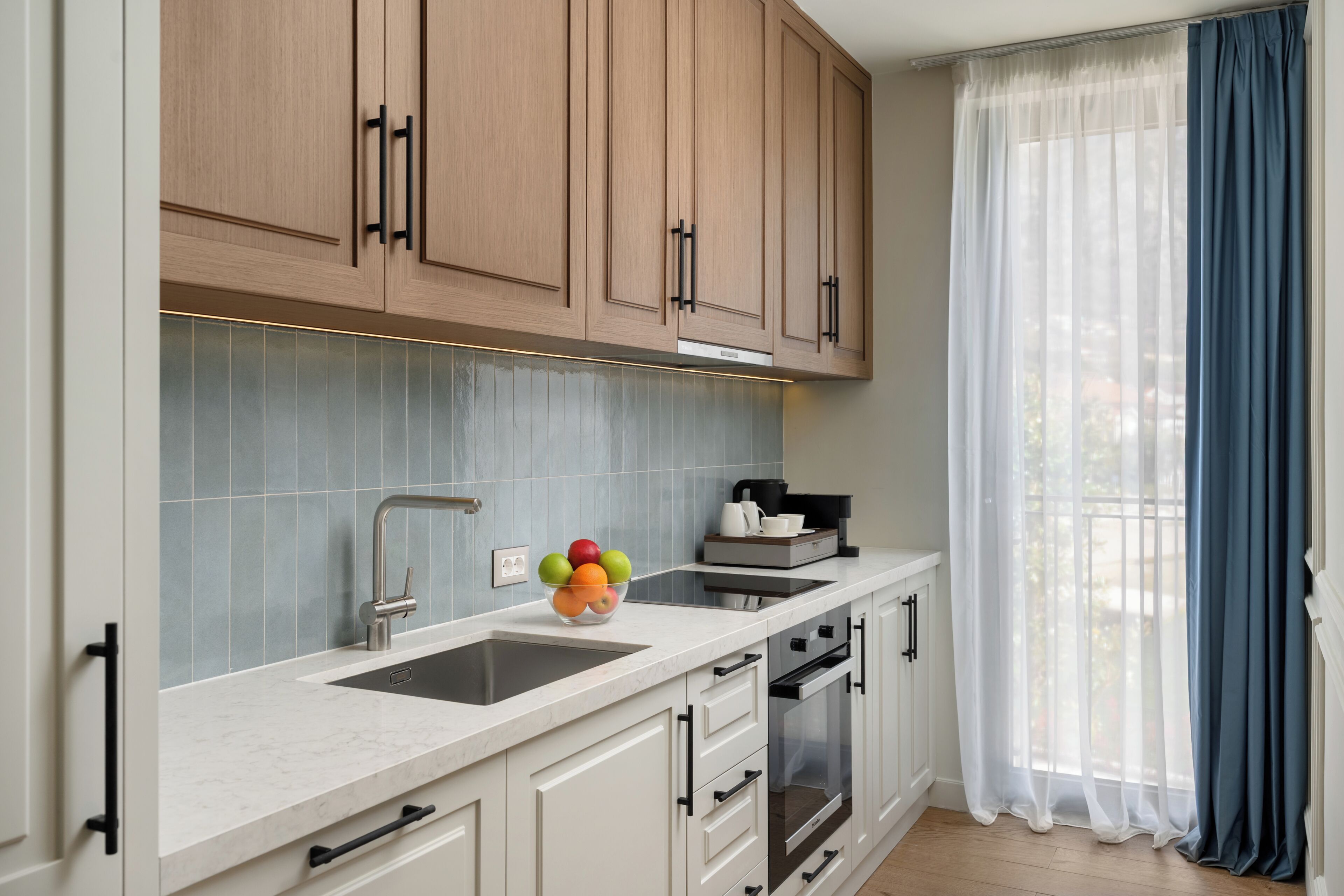 A modern kitchen with wooden cabinets, a marble countertop, a sink, and a fruit bowl.