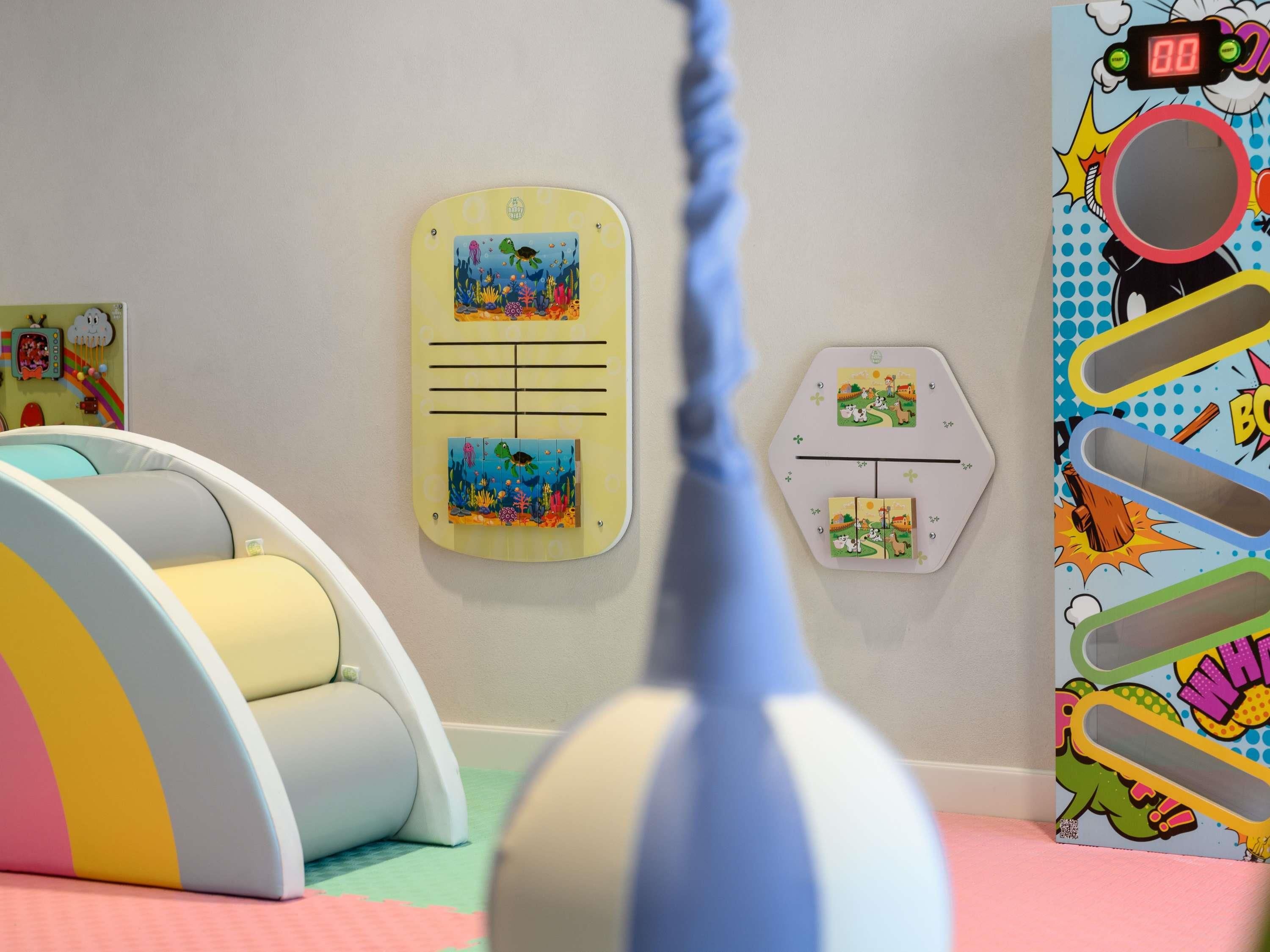 A children's play area with a colorful ball pit, a hanging toy, and wall decorations including a clock and a board with pictures.