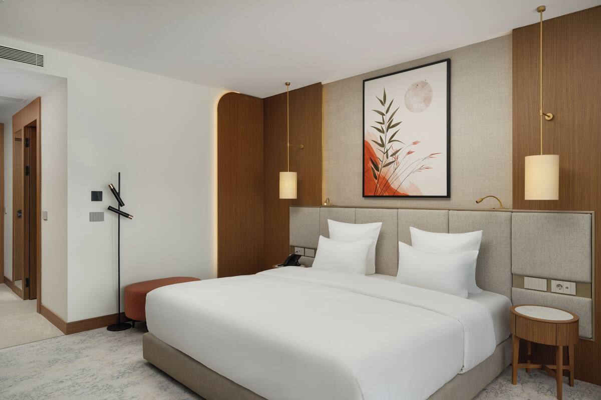 A hotel room with a large bed, a bedside table, a wall-mounted artwork, and a floor lamp.