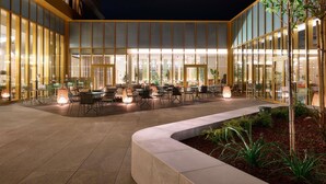 An outdoor seating area with tables and chairs, surrounded by glass walls and a building with vertical wooden panels. - Novotel Zagreb - opened September 2025 (Zagreb)