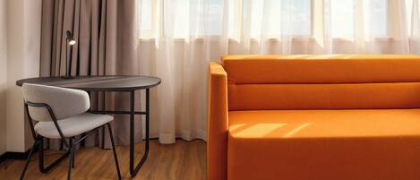 Una habitación moderna con piso de madera, una mesa redonda con una silla y un sofá naranja.