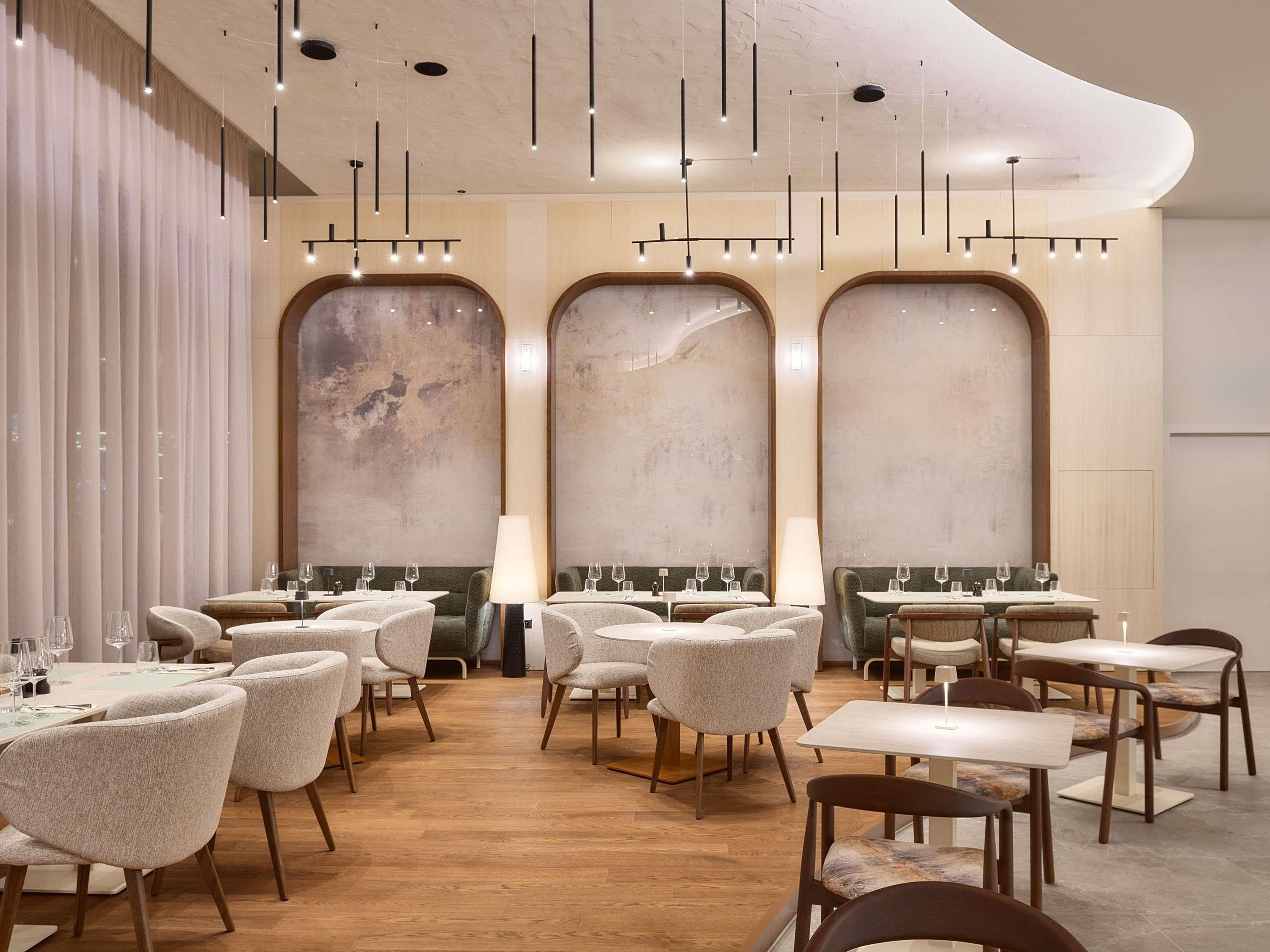 A restaurant interior with round tables, chairs, and hanging pendant lights.