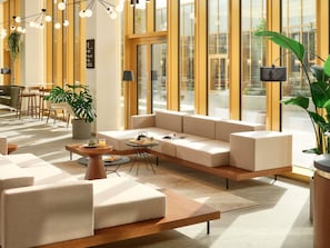 Un área de descanso moderna con sofá, mesa de centro y sillas, ventanas amplias y plantas de interior.