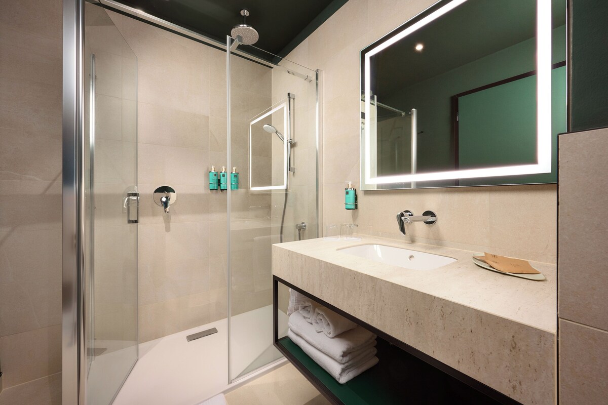 A modern bathroom with a glass-enclosed shower, a large mirror, and a vanity with a sink and towel rack.