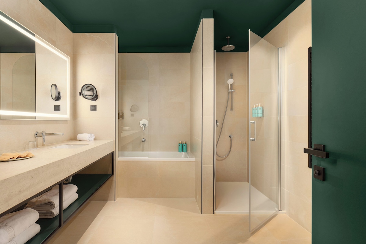 A modern bathroom with a glass-enclosed shower, a bathtub, and a vanity with a mirror and towel rack.