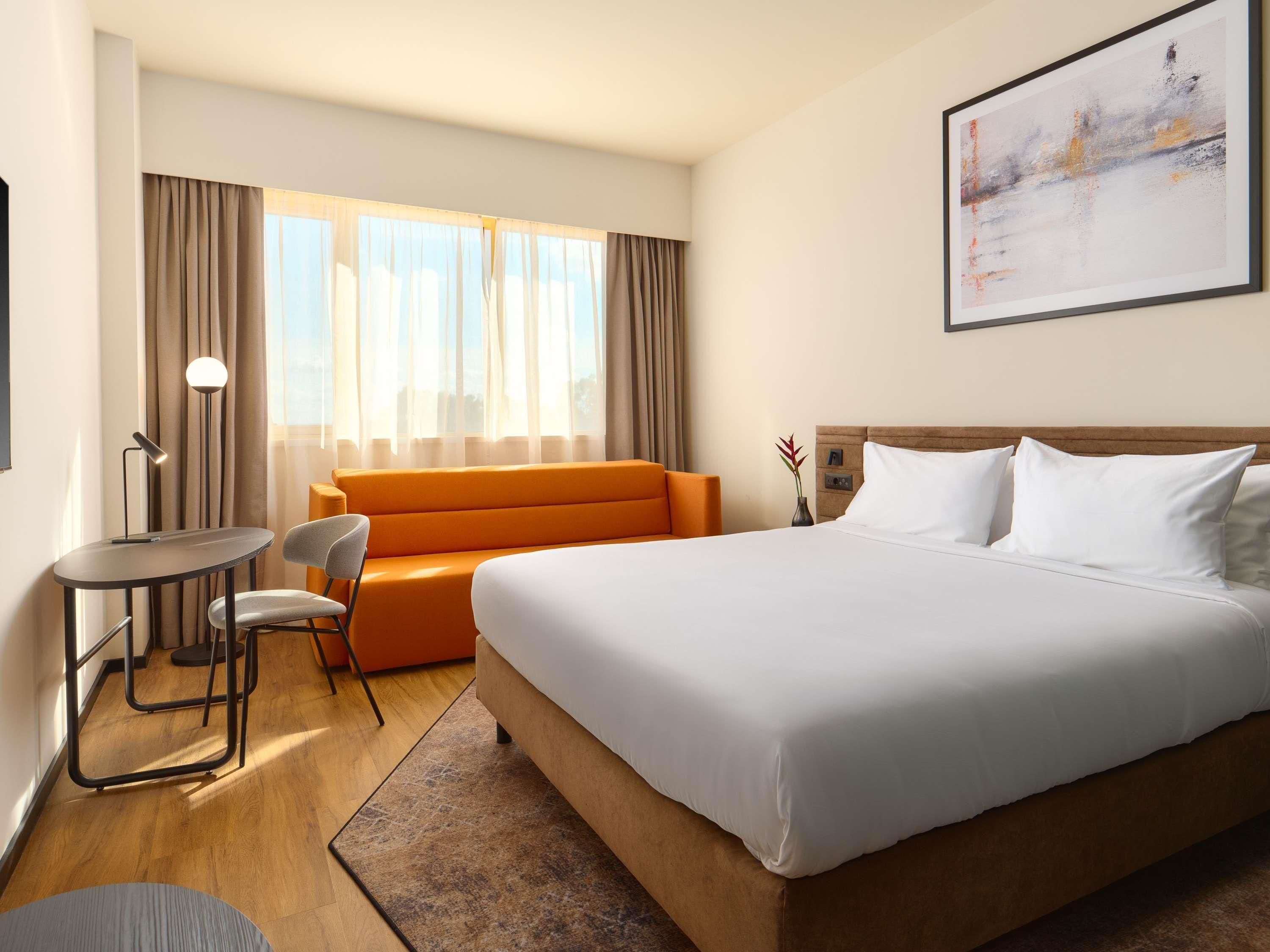 A hotel room with a large bed, a sofa, a small table, and a chair.