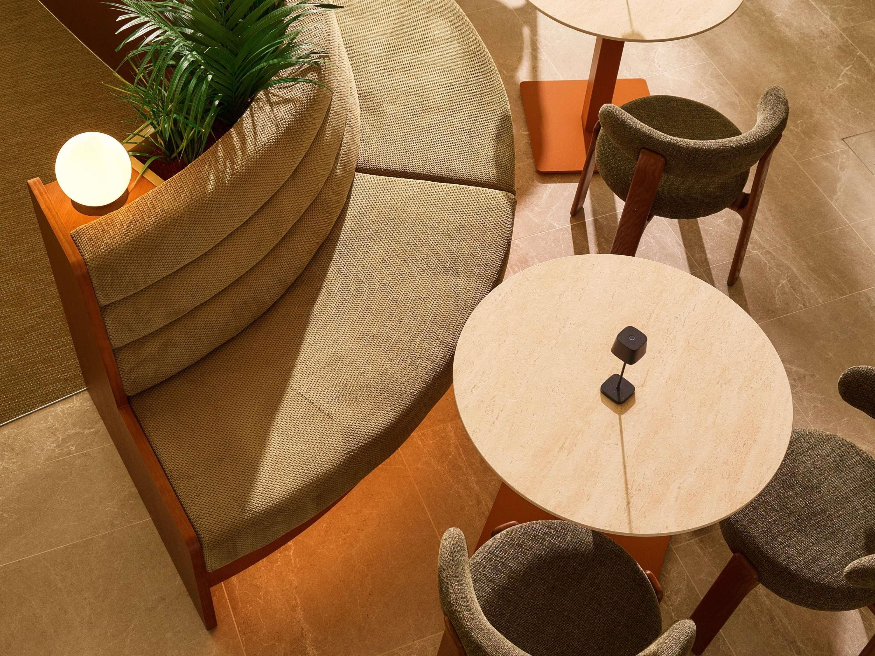 A modern lounge area with a round table, two chairs, a sofa, and a potted plant.