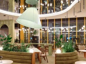 A modern interior with a curved ceiling, hanging pendant lights, and green upholstered seating. - Novotel Zagreb - opened September 2025 (Zagreb)
