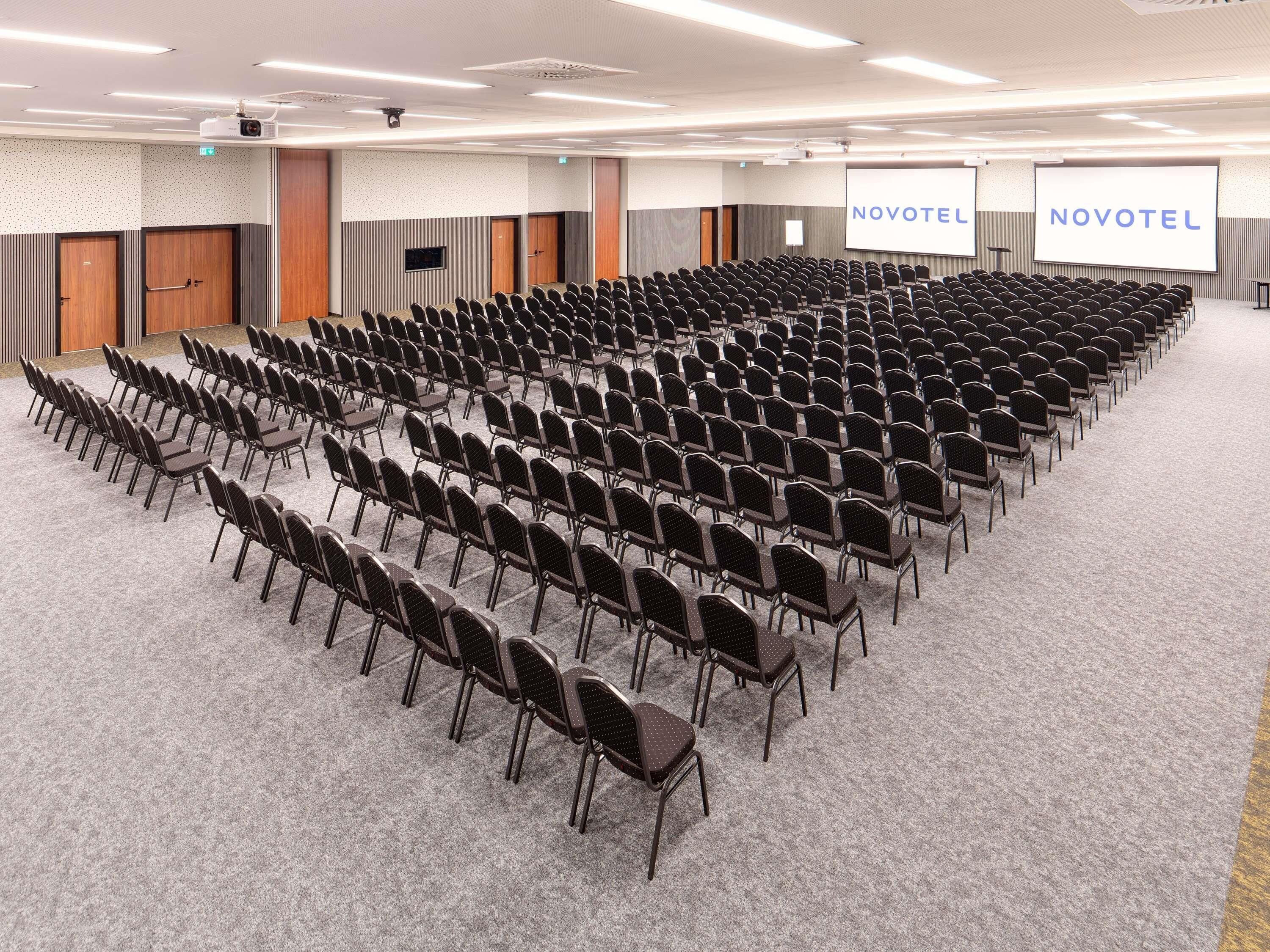 A conference room with rows of chairs, a projector, and a screen displaying 'NOVOTEL'.